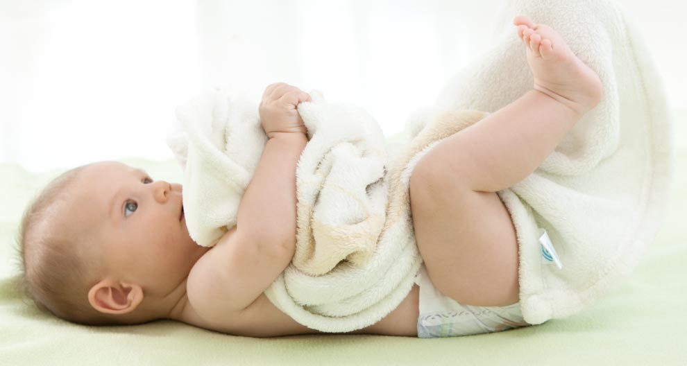 A baby lies on a green surface, wrapped in a white towel, with a diaper visible.