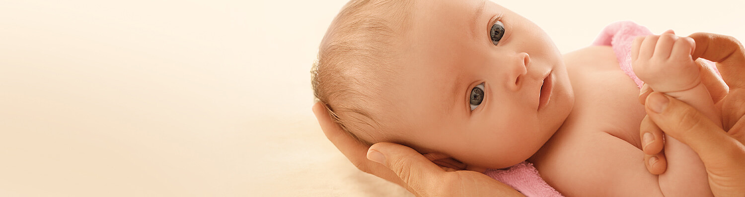A close-up of a baby's face and hands, held gently by an adult's hands.