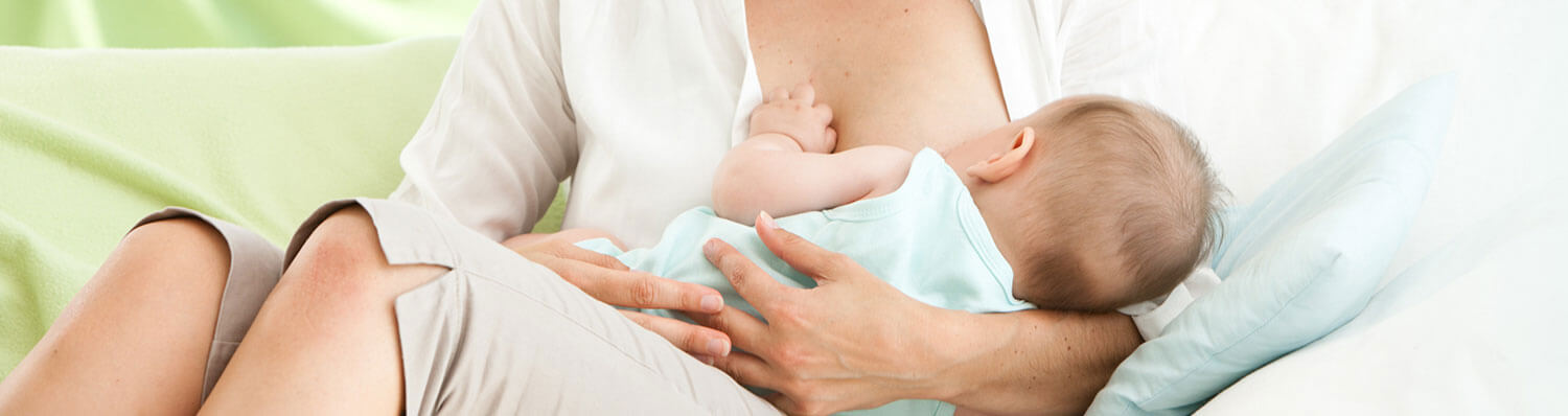 A woman in a white shirt is breastfeeding a baby.