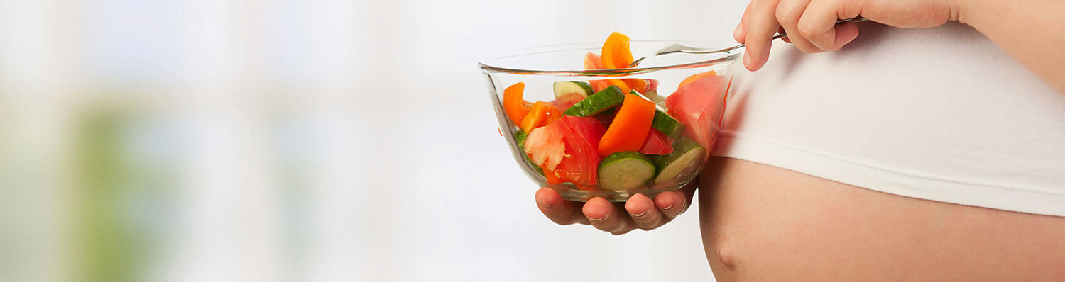A person is eating fresh vegetables from a glass bowl.