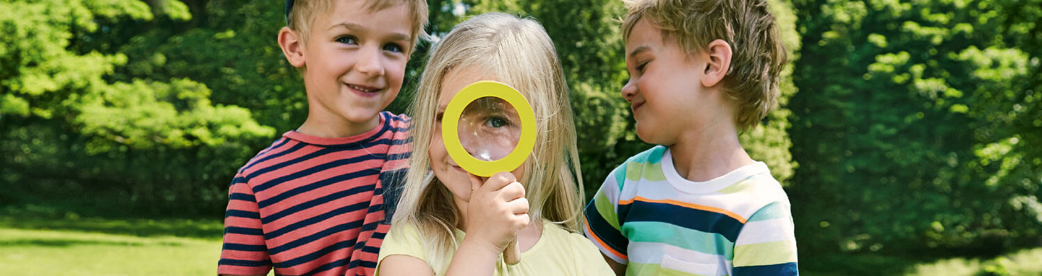 Three children outdoors, one holding a magnifying glass.