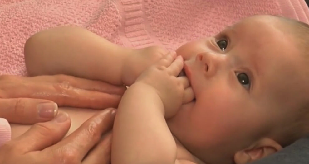 A baby with hands on face, lying on a pink towel.