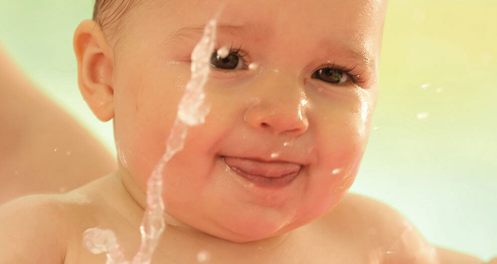 A baby's face is wet, with water droplets and a stream of water falling on the left side of the image.