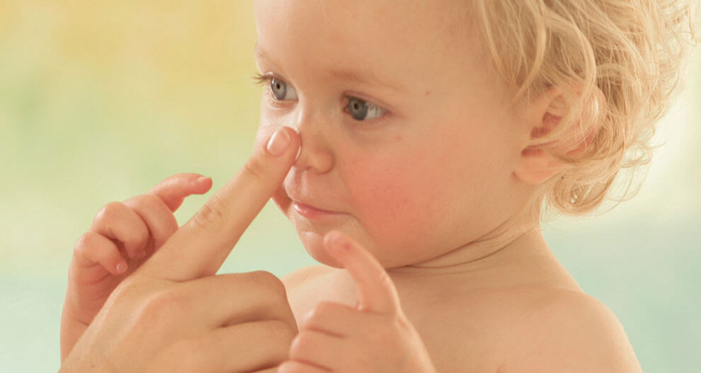 A child with curly hair is being held by an adult, who is touching the child's nose.