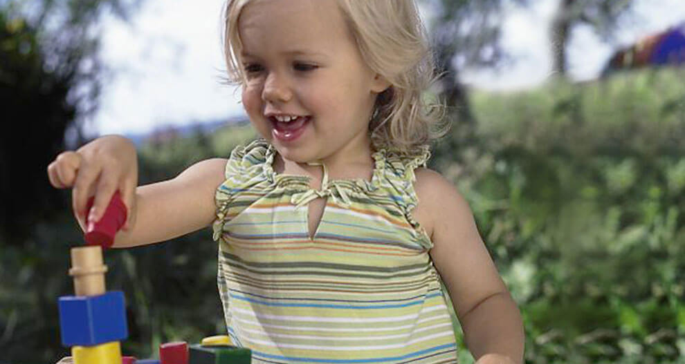 A young child is playing with colorful stacking blocks outdoors.