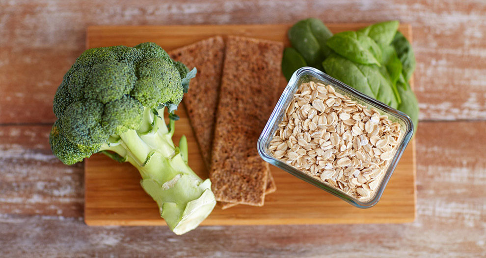 Broccoli, oatmeal, spinach, and bread on a wooden surface.
